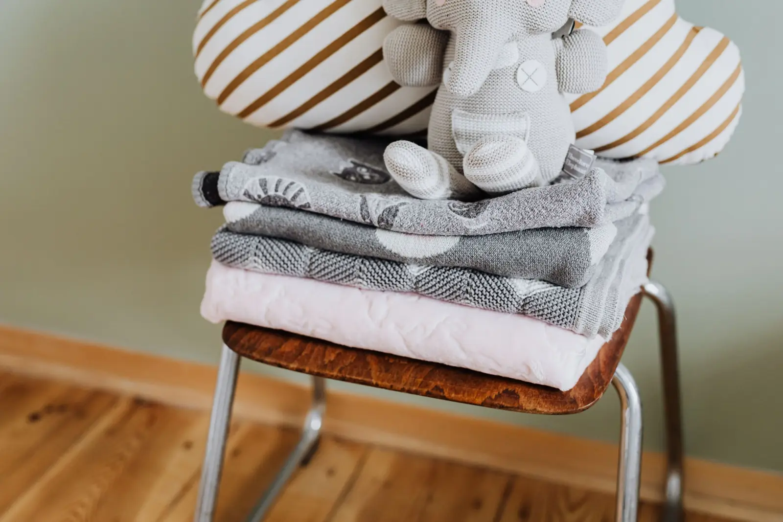 Folded baby blankets and a knitted elephant on a wooden chair