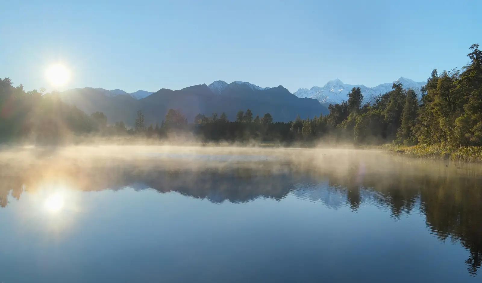 A still lake at sunrise with mist on the water and mountains behind