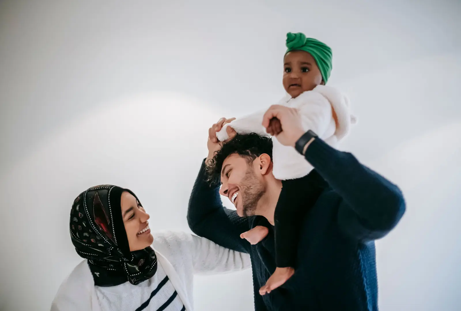 Parents laughing as the father carries their baby on his shoulders